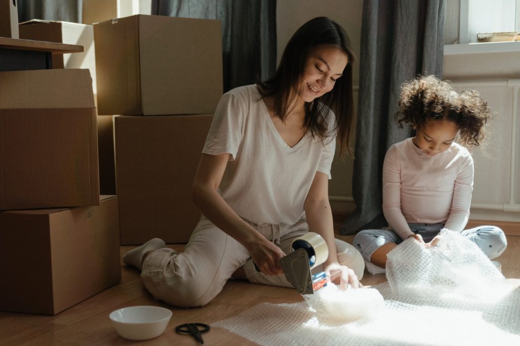photo of woman and child surrounded by moving boxes, packing items in bubble wrap and tape