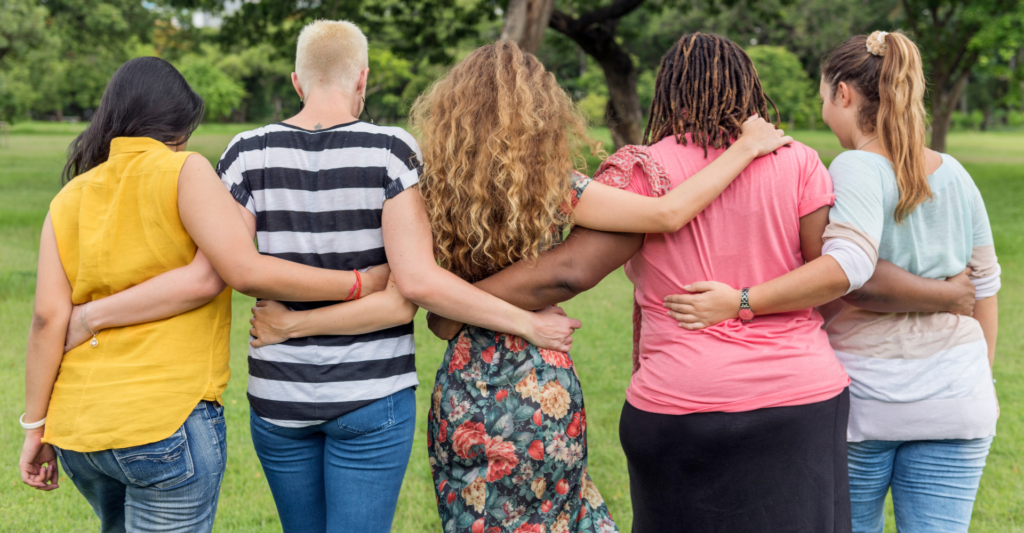 group of women of different sizes and ethnicies with linked arms, facing away from the camera