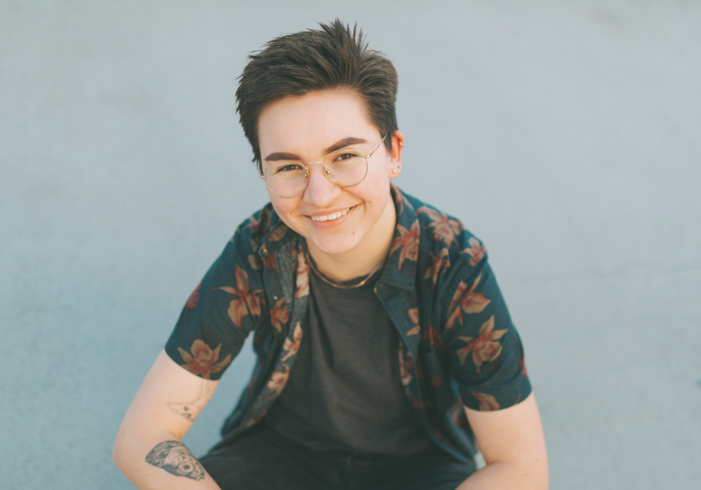 portrait of young trans man with glasses smiling at the camera