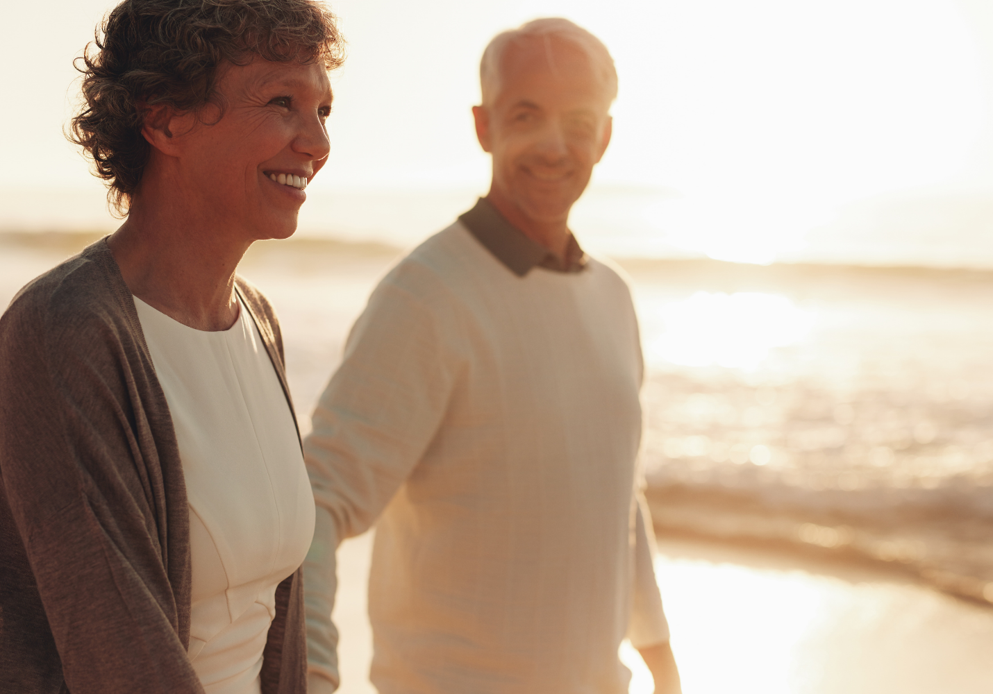 older white couple walks along a beach