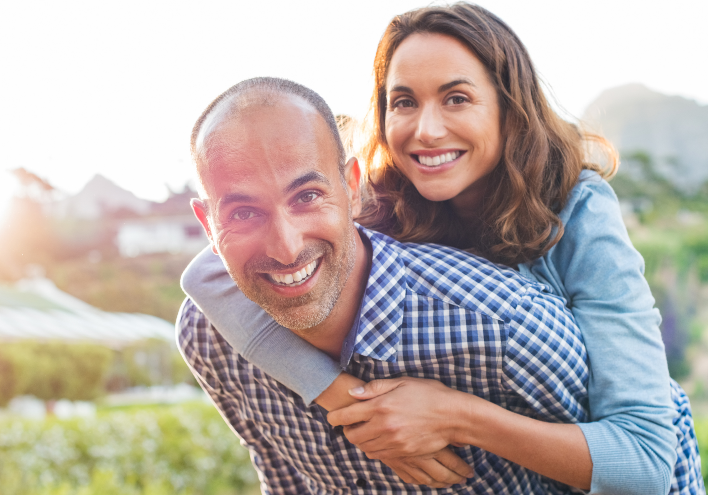 white couple smiling at the camera, woman with brown hair piggyback on a man with close-cropped hair