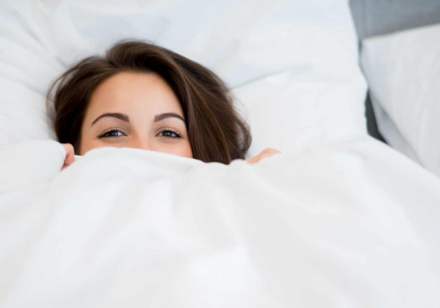 smiling white woman with brown hair under a white duvet pulled up to her eyes