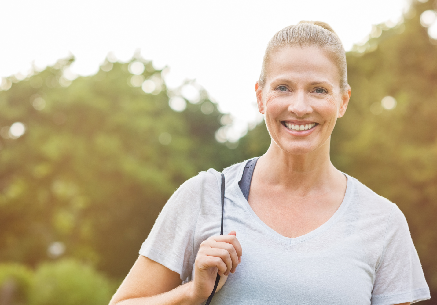 blonde white woman with a ponytail carrying a yoga mat