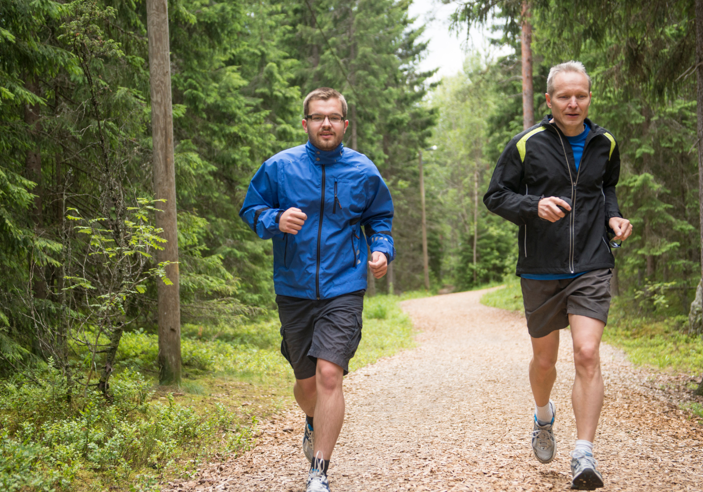 two middle aged white men jog on a wooded path