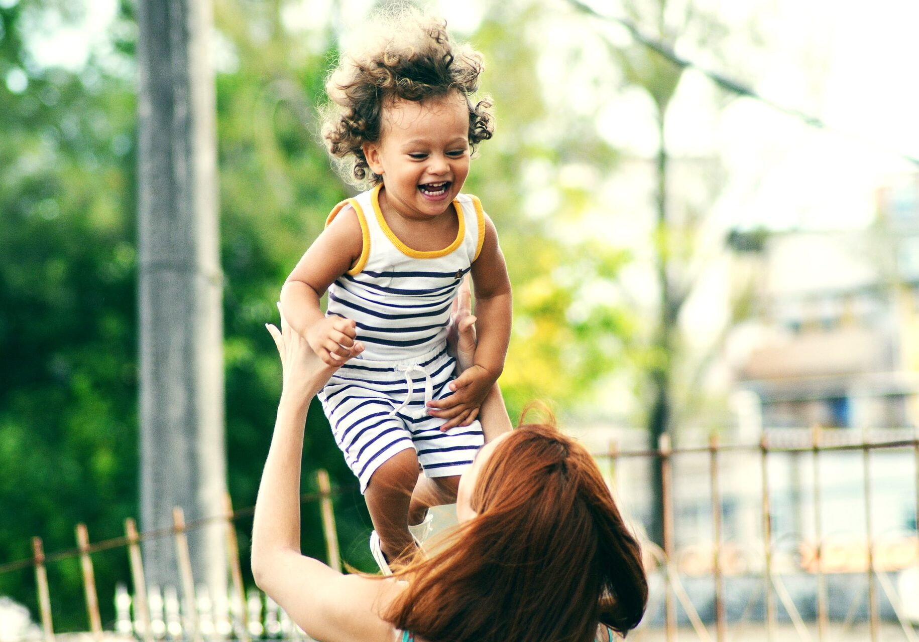 white woman seen from behind tosses a giggling, curly-haired toddler in the air